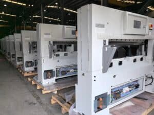 Row of new hydraulic paper cutting machines in warehouse with electrical control panels open for inspection and wiring verification.
