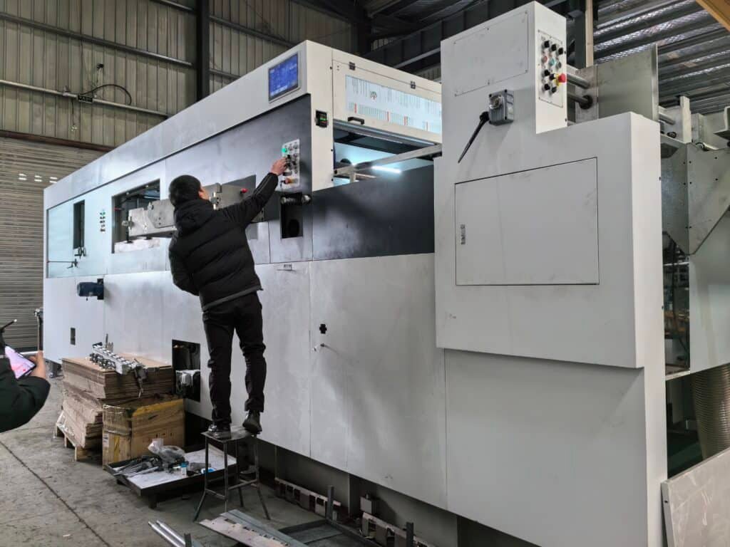 Technician performing safety and functionality tests on the control panel of a large format automatic die cutting machine before delivery.