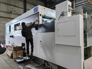 Technician performing safety and functionality tests on the control panel of a large format automatic die cutting machine before delivery.