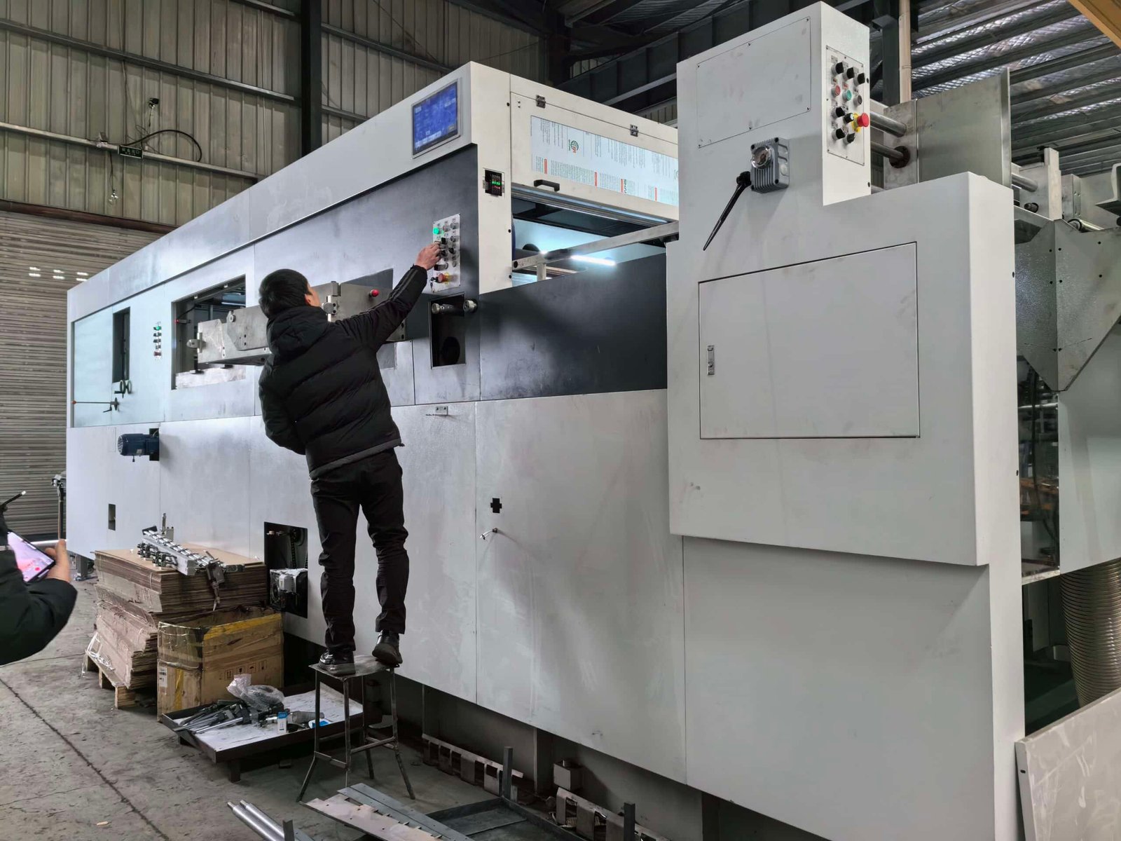 Technician performing safety and functionality tests on the control panel of a large format automatic die cutting machine before delivery.