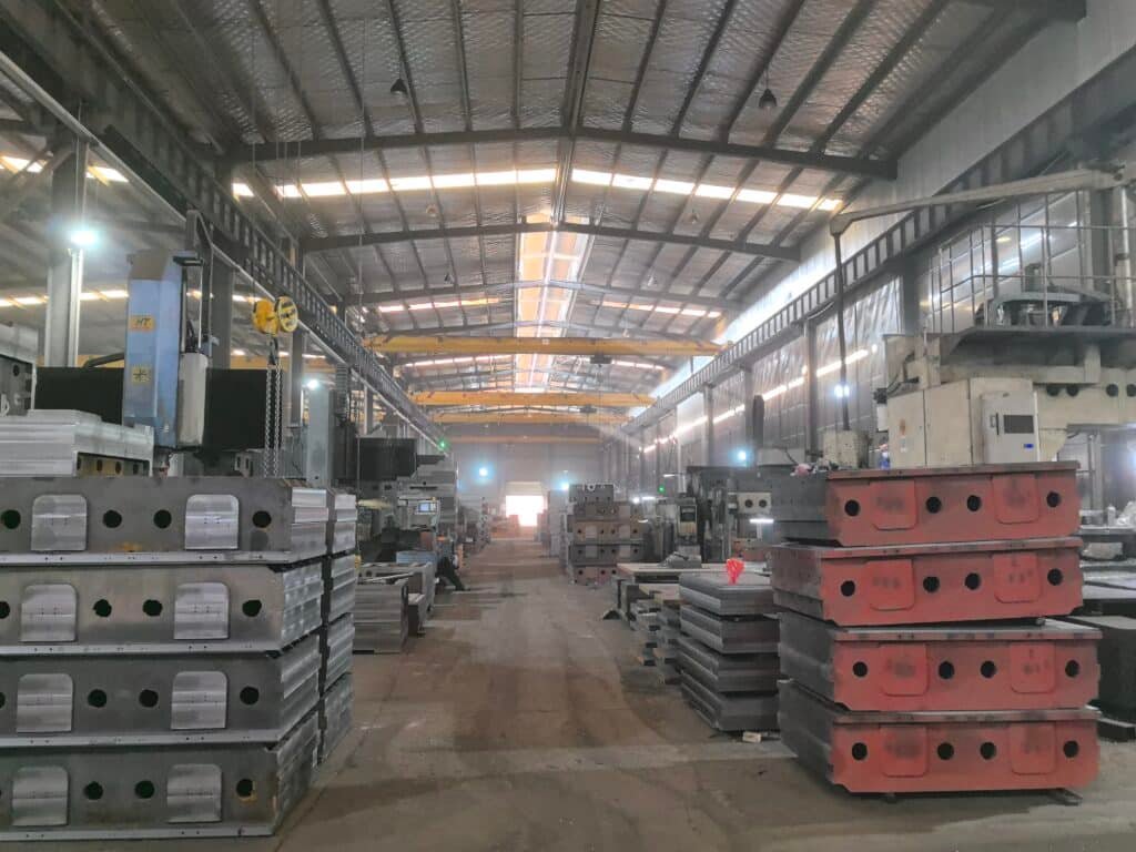 Stacks of heavy-duty steel chase plates and molds in a die cutting machine manufacturing facility, waiting for assembly or quality check.