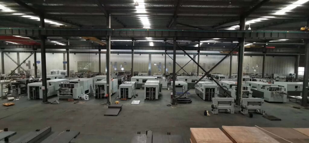 Wide view of a large manufacturing facility filled with rows of new automatic die cutting machines ready for shipment to packaging factories.