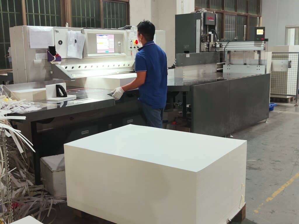 Operator loading a large stack of paper into a modern DAIS servo-driven paper cutting machine in a printing factory production line.