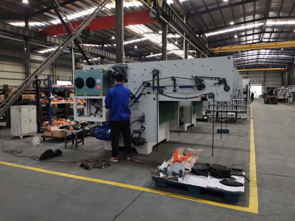 Professional technician conducting preventive maintenance on industrial cutting machinery in a factory workshop, inspecting internal drive chains and mechanical components.