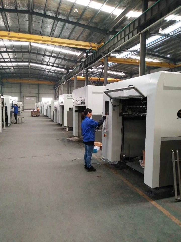 Operator performing maintenance and setup on a DAIS automatic die cutting machine in a modern printing machinery factory.