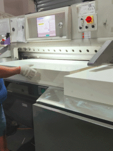 operator feeding paper into servo-driven automatic paper cutting machine with PLC touch-screen interface