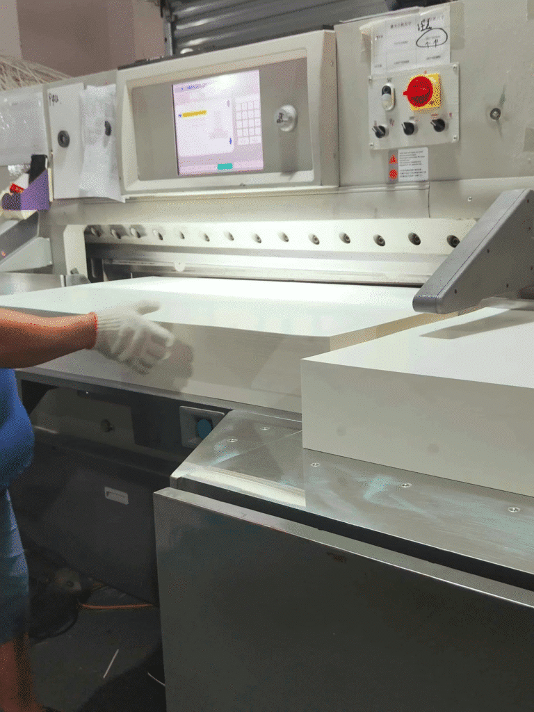 operator feeding paper into servo-driven automatic paper cutting machine with PLC touch-screen interface