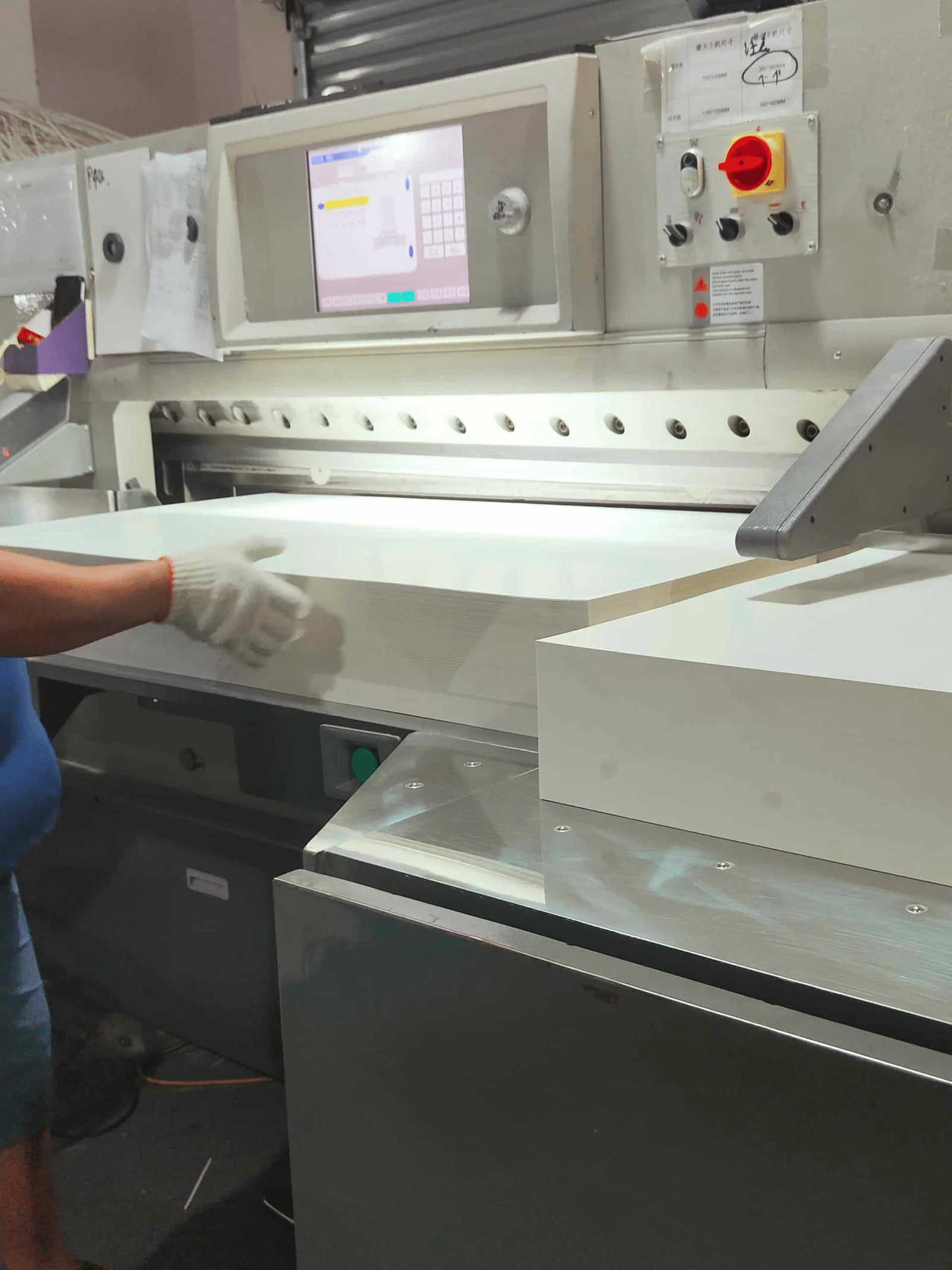 operator feeding paper into servo-driven automatic paper cutting machine with PLC touch-screen interface