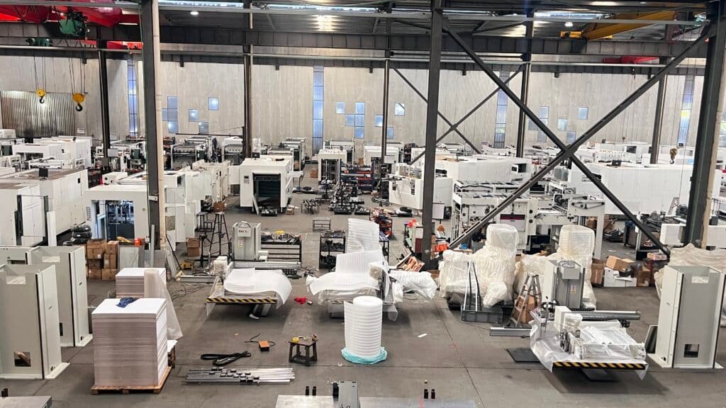 A large printing and packaging factory floor with multiple paper cutting machines and other post-press equipment, demonstrating large-scale production capacity.