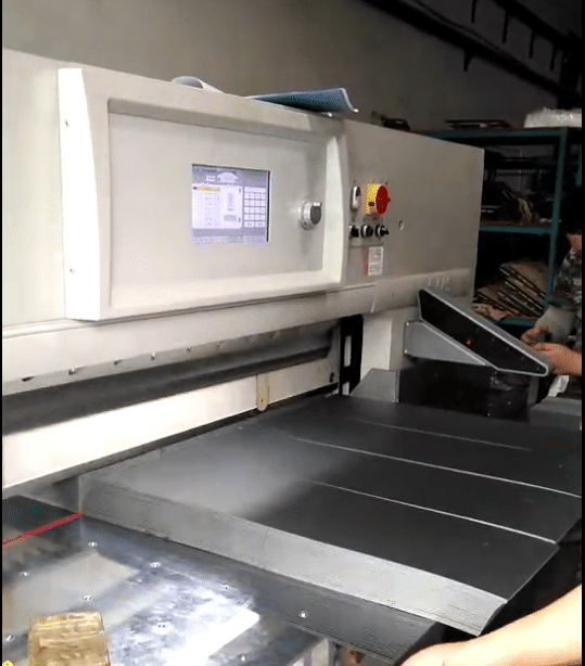 An operator programming and operating a paper cutter using its color touch screen control panel, demonstrating the machine's high level of automation.