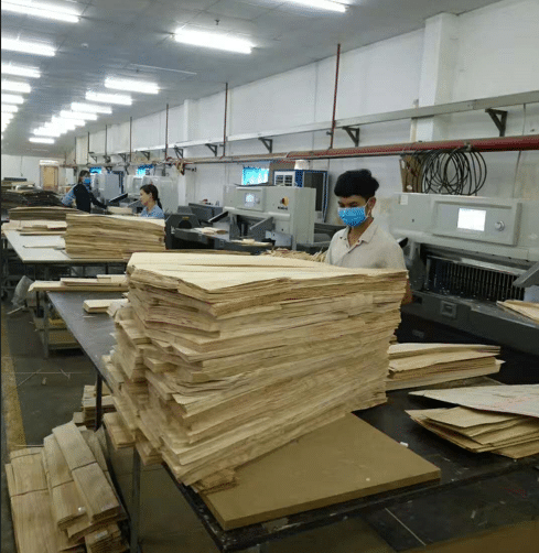 A worker handling a large stack of thick paperboard, preparing for cutting on a paper cutter, demonstrating the need for high stack capacity and heavy-duty material handling.