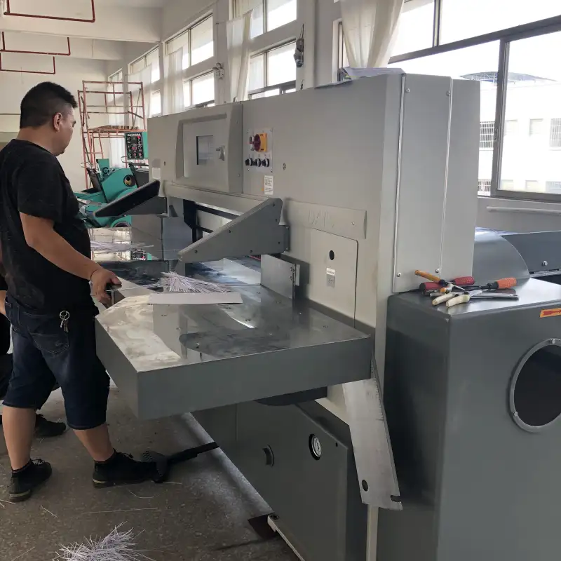 Operator inspecting paper stack on a hydraulic guillotine cutting machine.