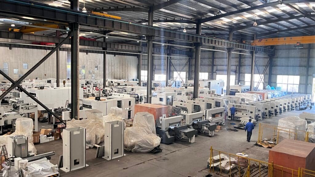Warehouse filled with newly manufactured paper cutting machines, ready for shipment to printing and packaging facilities worldwide.