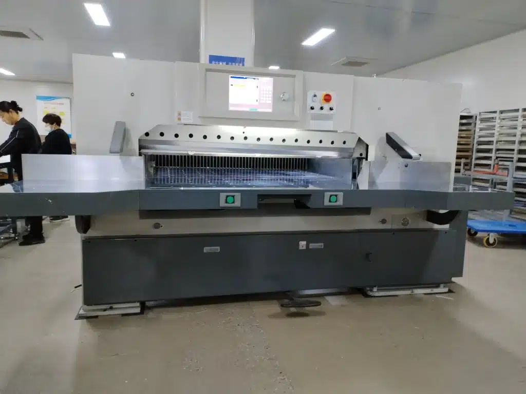 Front view of paper cutting machine with visible safety light barriers and dual-hand controls for operator protection