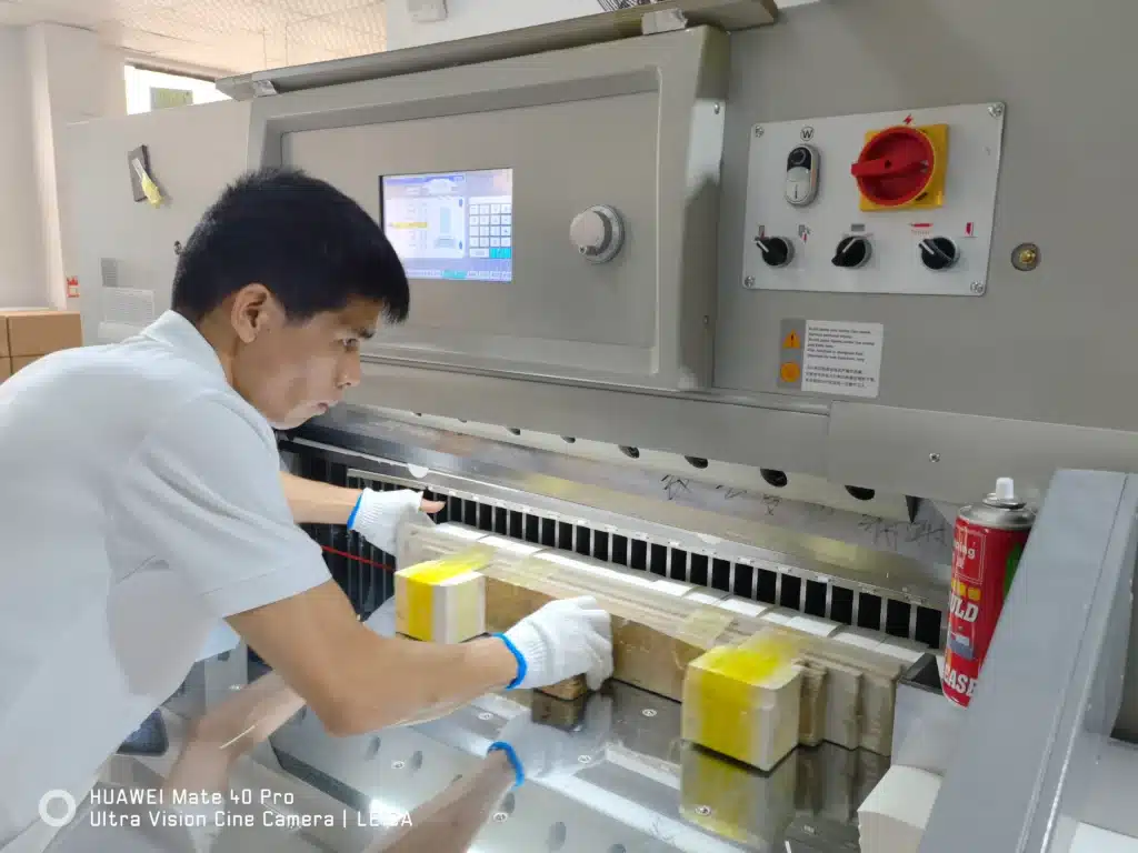 Operator manually aligning paper stack on programmable hydraulic paper cutter for packaging production