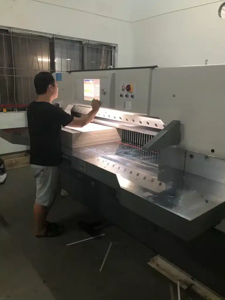 Operator using a CNC hydraulic paper cutting machine with touchscreen interface for precise stack alignment