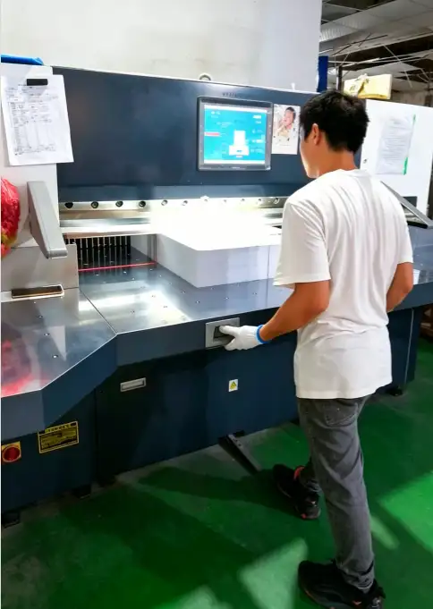 Operator wearing gloves operating paper cutter with clamped stack to prevent movement during cut