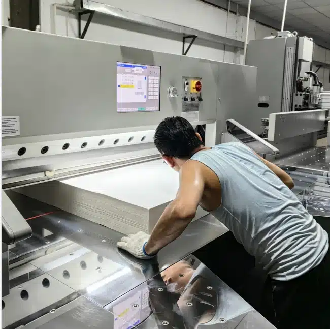Worker operating programmable hydraulic cutter with touchscreen interface for thick board packaging materials