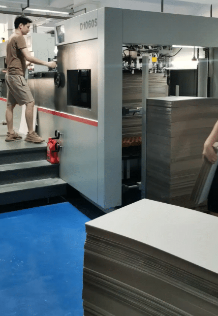 Operator adjusting settings on DAI'S D1060S automatic flatbed die cutting machine during setup.