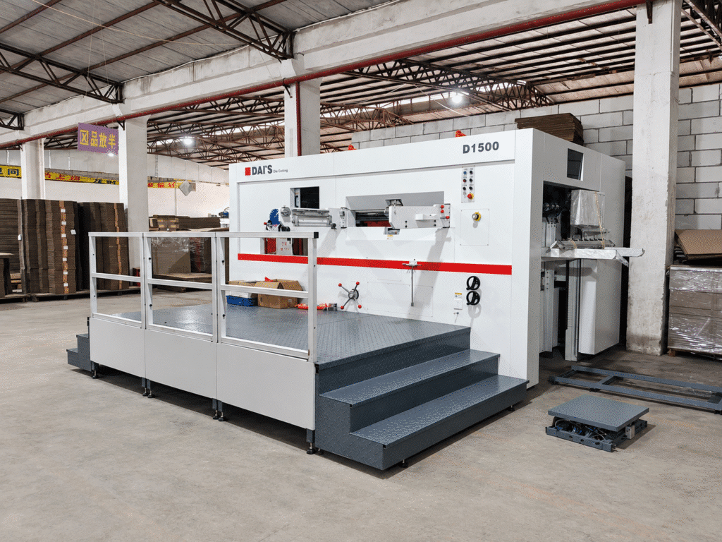 Semi-automatic flatbed die cutter operating in a packaging plant with sheets in process and finished blanks, illustrating the gap between rated speed and actual saleable output