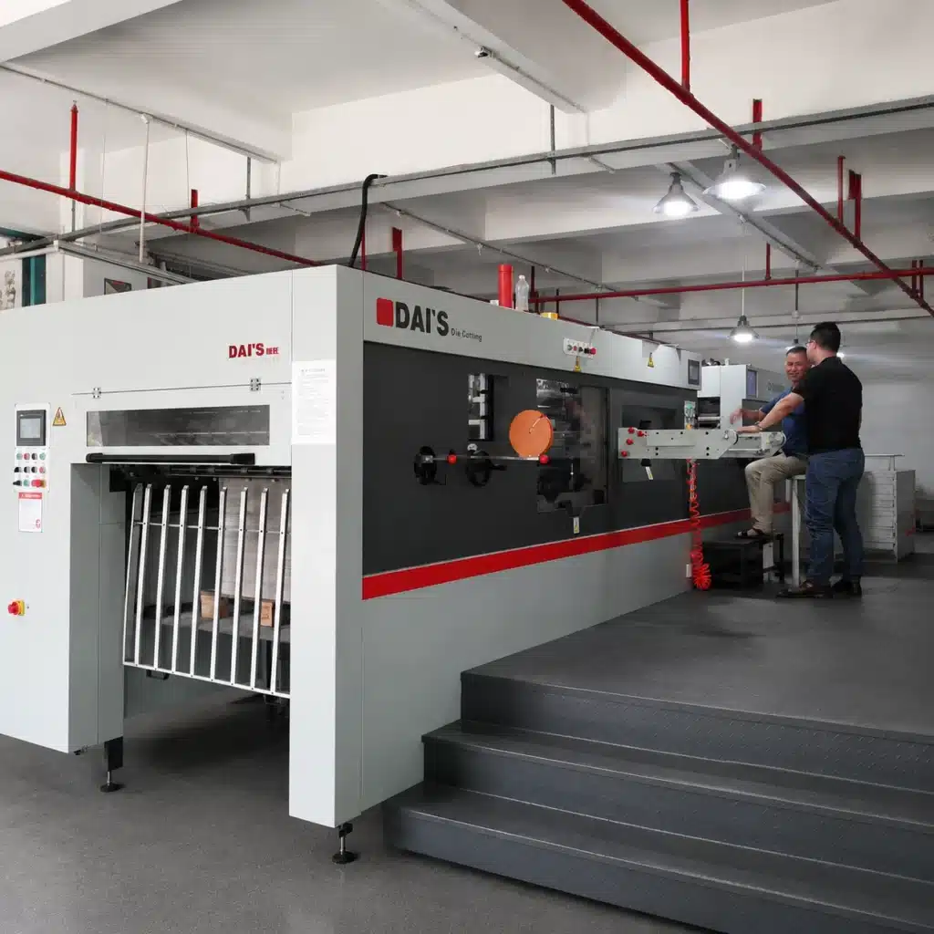Semi-automatic flatbed die cutting machine in an industrial packaging plant, showing machine scale and paperboard production context